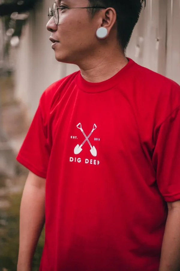 Male model wearing red Mucky Shovel graphic T-shirt, front view.
